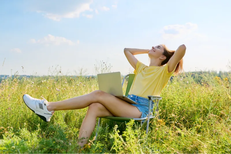 Ragazza felice seduta in mezzo a un prato, con un pc appoggiato sulle gambe