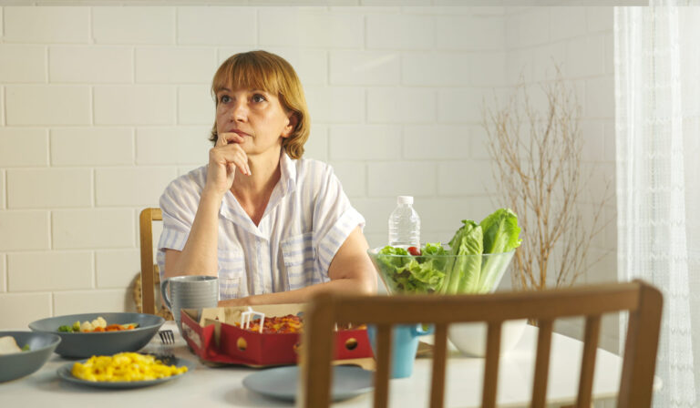 Donna a tavola pensierosa che mangia alimenti per assorbire meglio il ferro.